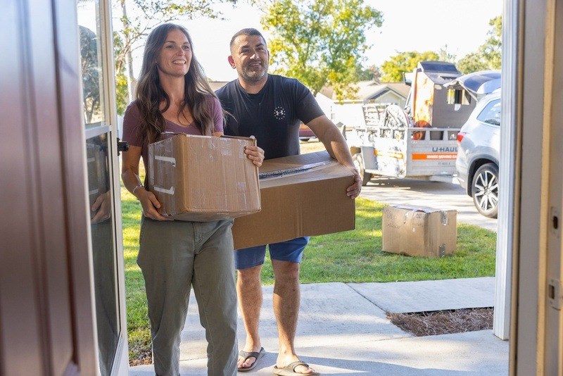 A man and a woman are carrying a box out of a house.