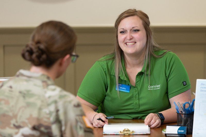 A woman in a green shirt is sitting at a table with a woman in a camouflage shirt.