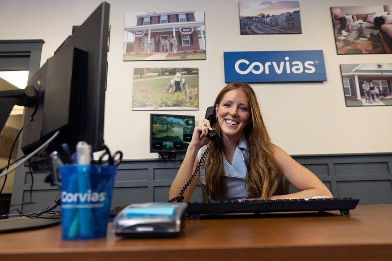 A woman is talking on the phone in an office with a Corvias logo on the wall.