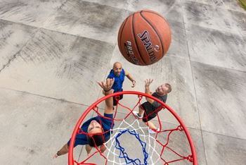 A basketball is in mid-air, about to be dunked into the hoop by a man in a blue shirt.