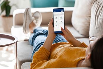 A person in a yellow sweater is lying on a couch using a tablet.