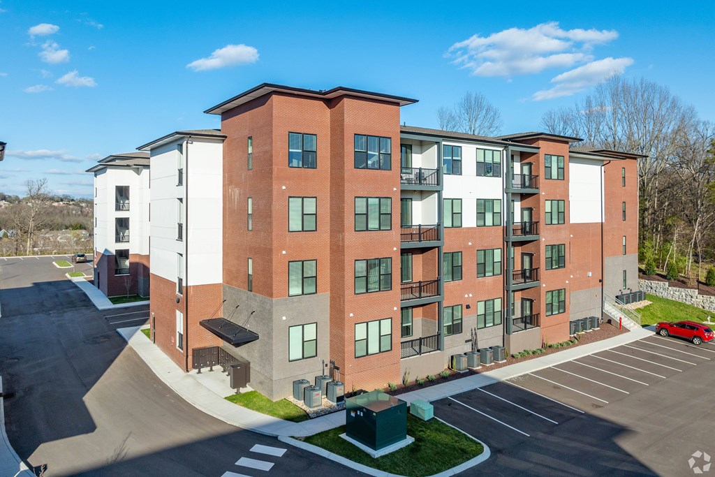 A red car is parked in the parking lot of a multi-story apartment building.