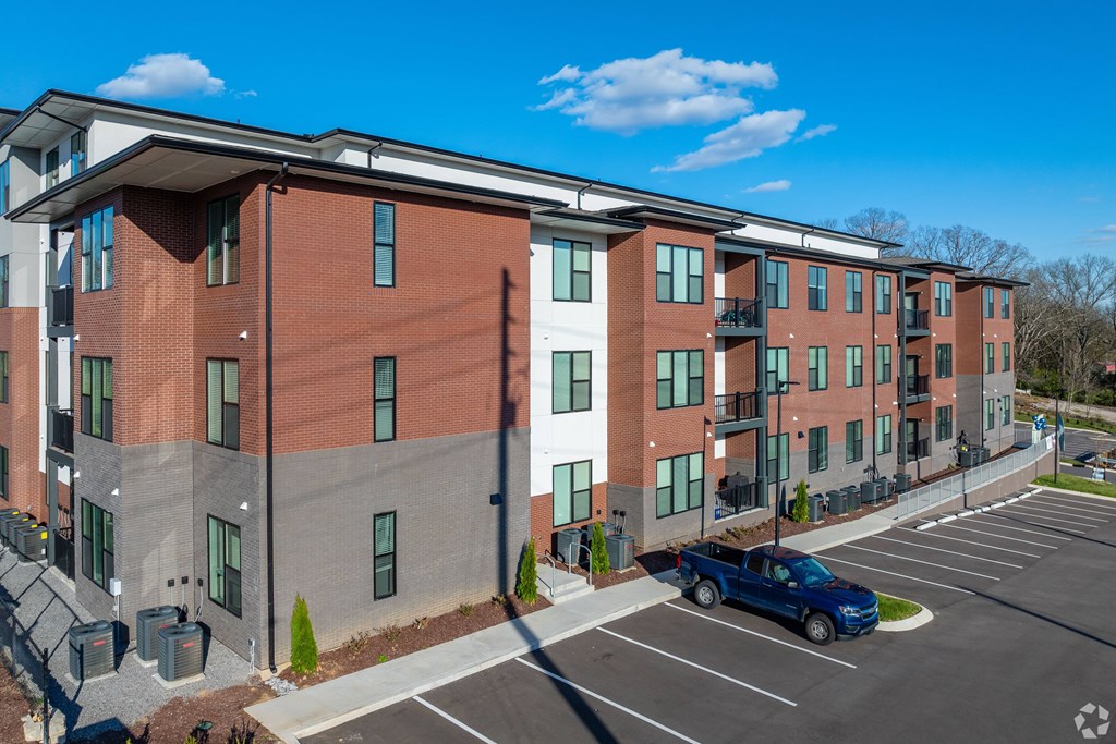 A blue truck is parked in a parking lot in front of a red and grey building.