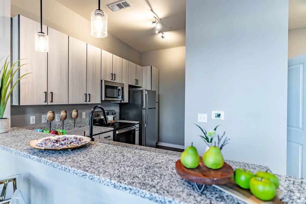 A kitchen with granite countertops and a tray of green apples.