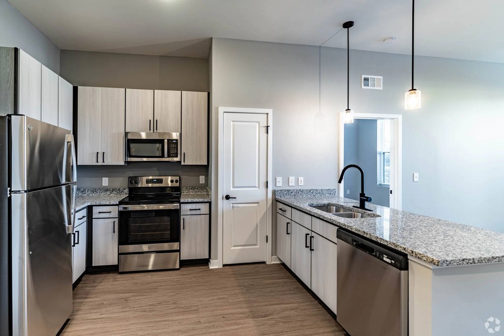 A kitchen with a refrigerator, oven, microwave, sink, and cabinets.