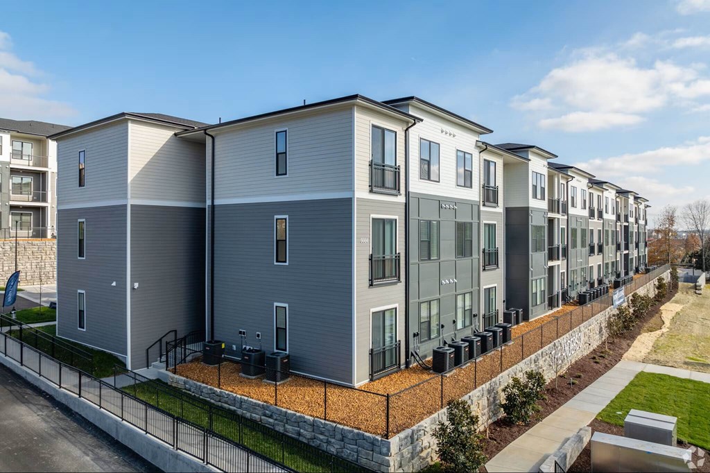 A row of modern townhouses with a sidewalk and landscaping in front.