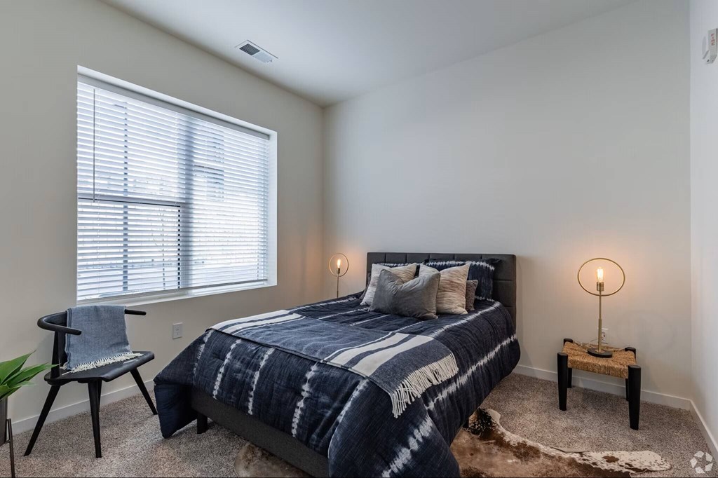 A bedroom with a bed, chair, and lamp.