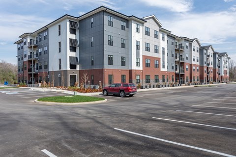 A red car is parked in a parking lot in front of apartment buildings.