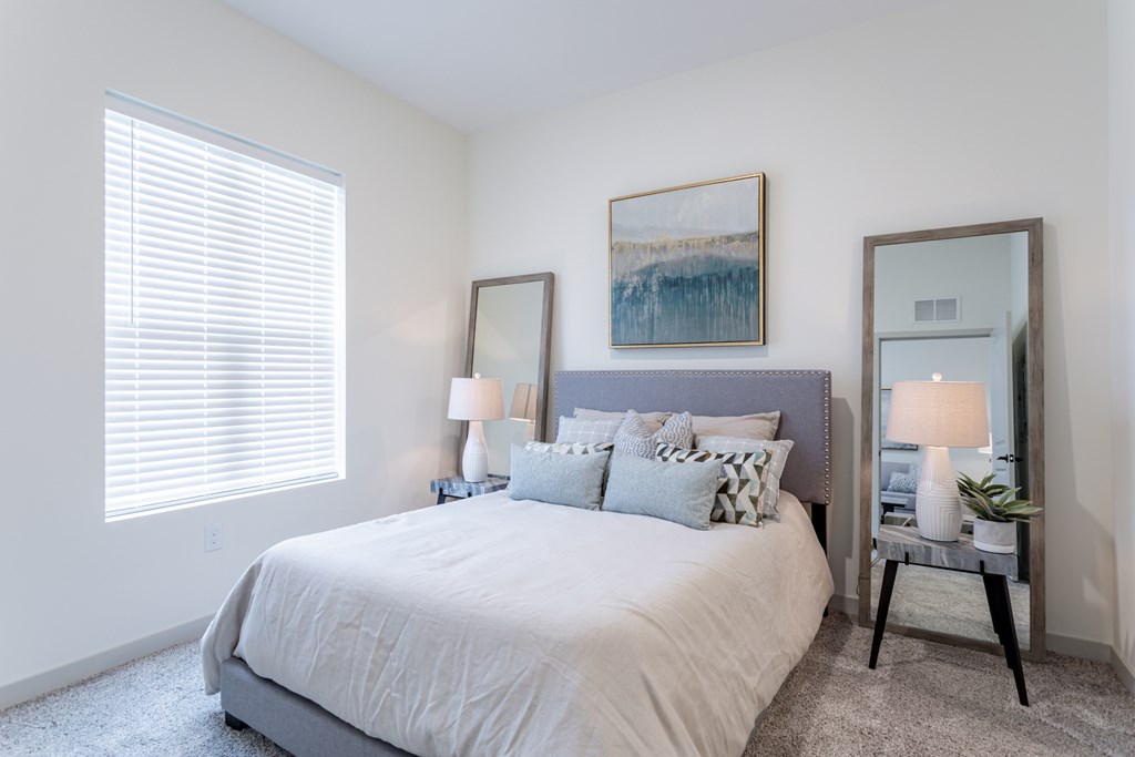A bedroom with a large bed, two lamps, and a painting on the wall.