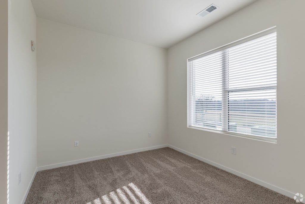 A room with a carpeted floor and a window with blinds.
