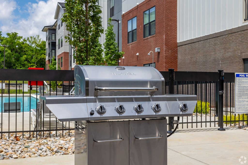 A silver gas grill with four burners is in front of a black fence.