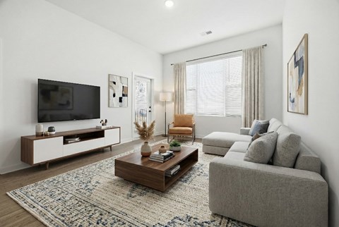 A modern living room with a grey sofa, a wooden coffee table, and a television on a white cabinet.