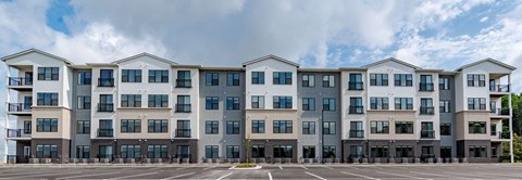 A large, modern apartment building with multiple balconies and a parking lot in front.