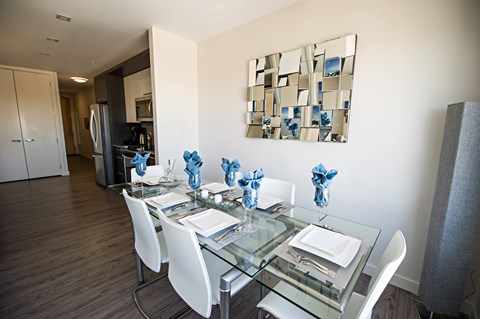 A modern dining room with a glass table and white chairs.