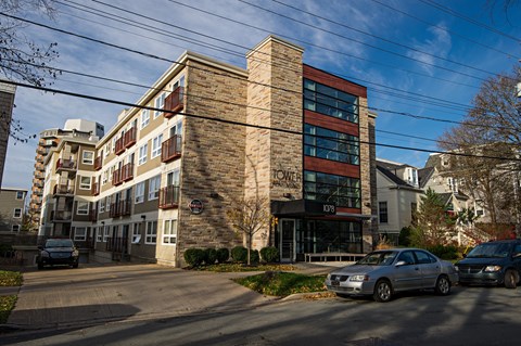 A modern building with a brick facade and a glass entrance is surrounded by parked cars.