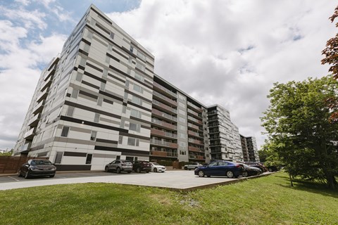 A modern building with a grassy area in front and cars parked along the side.