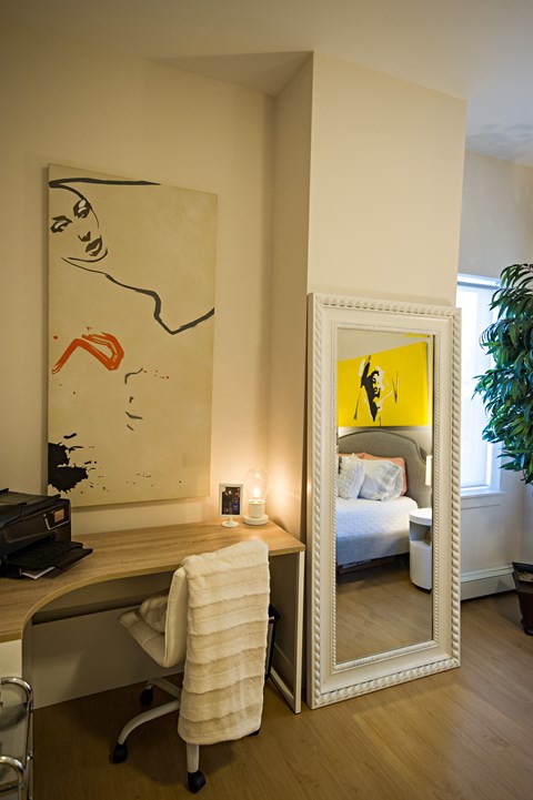 A large mirror reflects a bedroom with a bed and a plant.