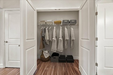 A white closet with clothes hanging and baskets on the floor.