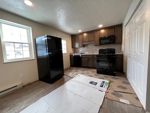 A kitchen with a black fridge, microwave, and oven with cabinets and a window.