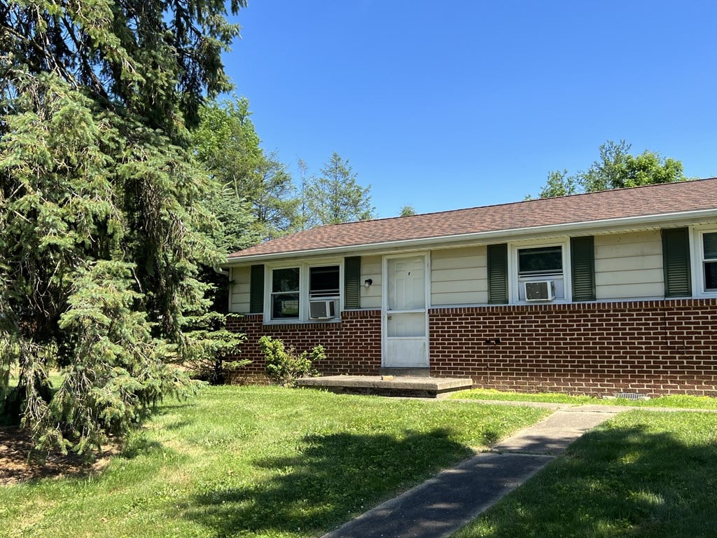 A house with a white door and windows is surrounded by greenery.