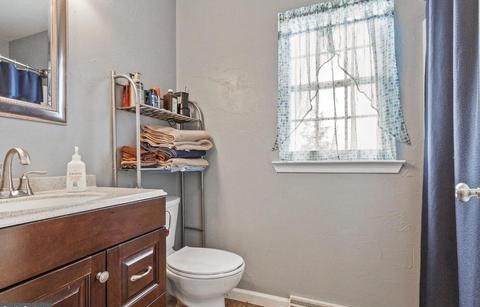 A bathroom with a toilet, sink, and a window with a curtain.