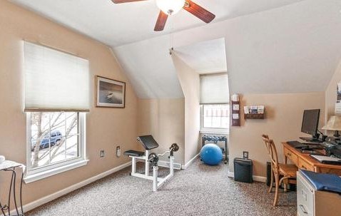 A room with a fan, a chair, a table, and a window.