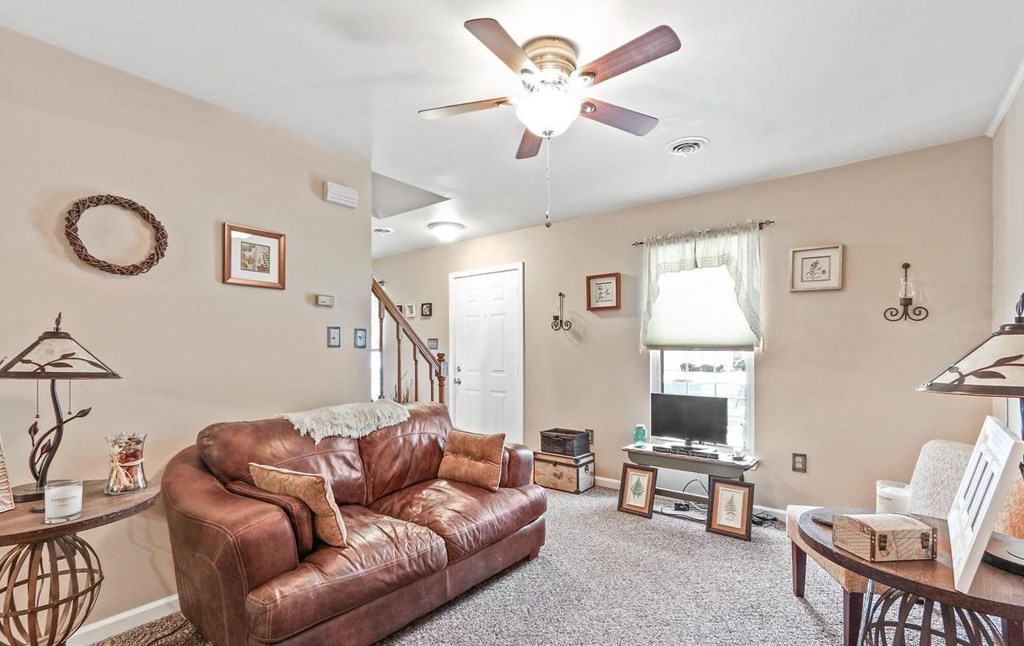 A living room with a brown leather couch and a ceiling fan.