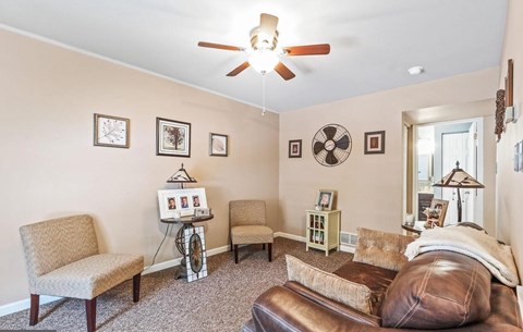 A living room with a brown leather couch, a fan, and a table with a picture frame on it.