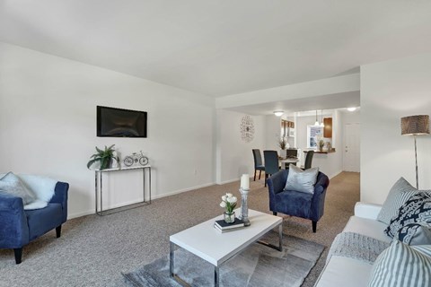A living room with a blue couch, a white coffee table, and a flat screen TV mounted on the wall.