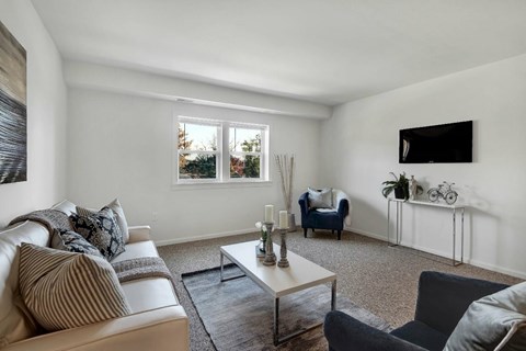 A living room with a white couch, a grey armchair, a coffee table, and a flat-screen TV mounted on the wall.