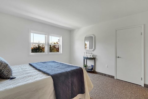 A bedroom with a bed, a nightstand with a mirror, and a window.