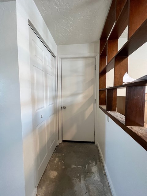 A white door is in a hallway with a brown shelf on the wall.