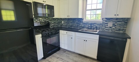 A black refrigerator is in a kitchen with white cabinets.