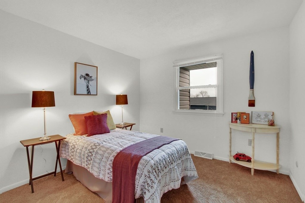 A bedroom with a bed, two lamps, a nightstand, and a window.