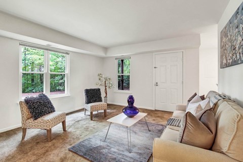 A living room with a white couch and a chair with a black pillow.