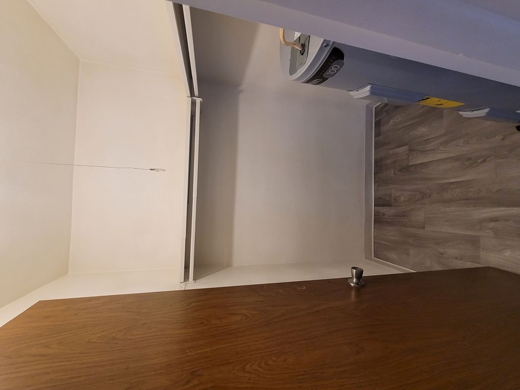 A room with a wooden floor and a white wall with a staircase.