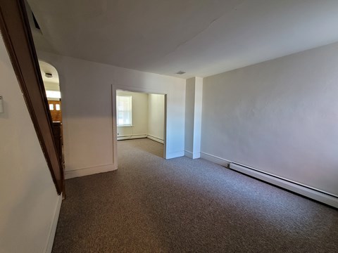 A carpeted room with white walls and a doorway leading to another room.
