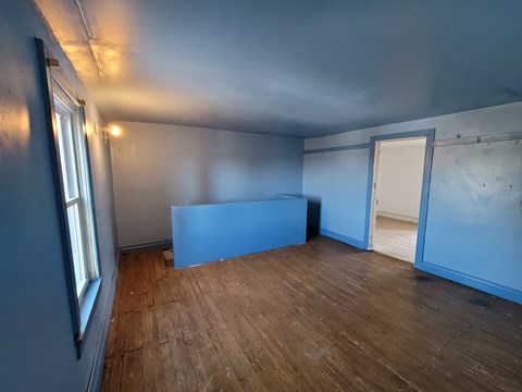 A room with wooden floors and a window on the left side.