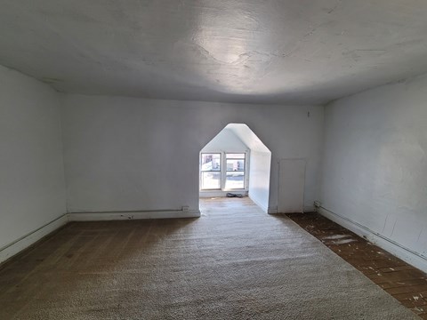 A room with a carpeted floor and a window at the end.