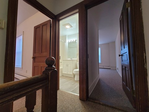 A hallway with a carpeted floor and a wooden railing.