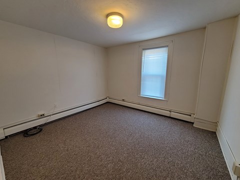 A room with a carpeted floor and a window with blinds.