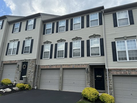 A grey house with black shutters and a black garage door.