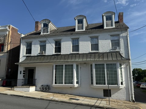 A white two-story house with a black roof and a black fence.