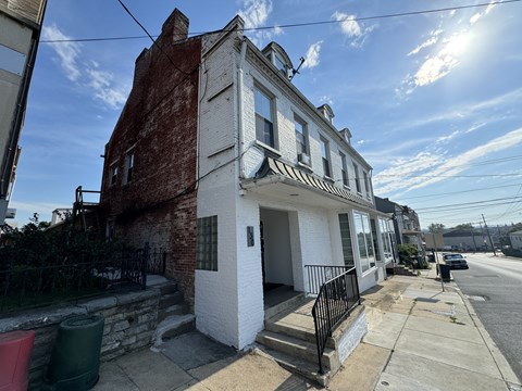A white house with a black iron fence is in front of a brick building.