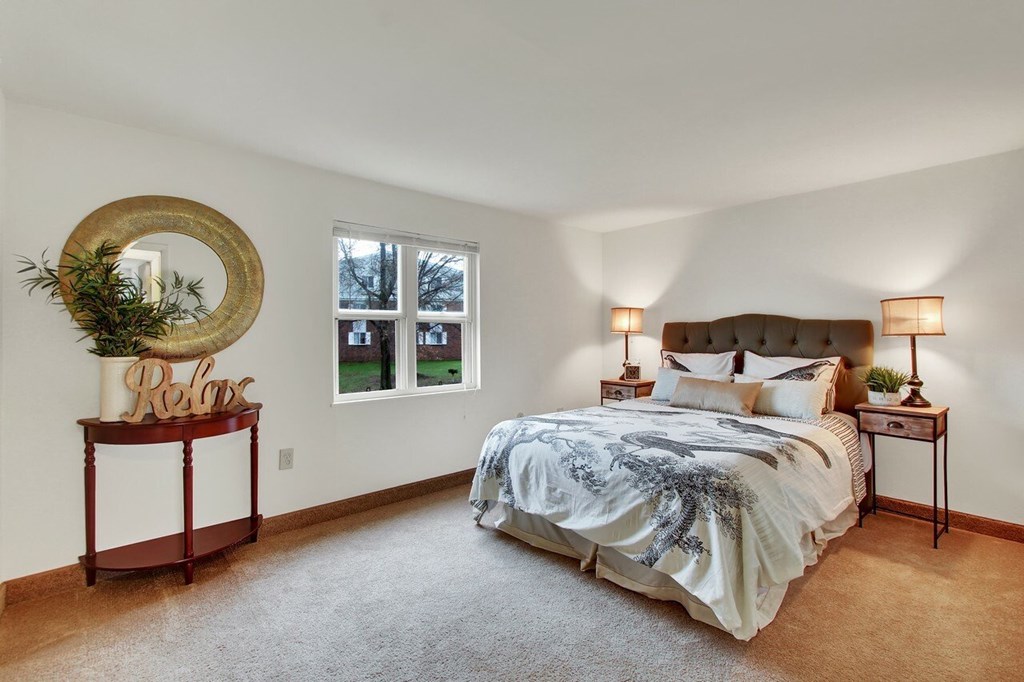 A bedroom with a large bed, a round mirror, and a potted plant.