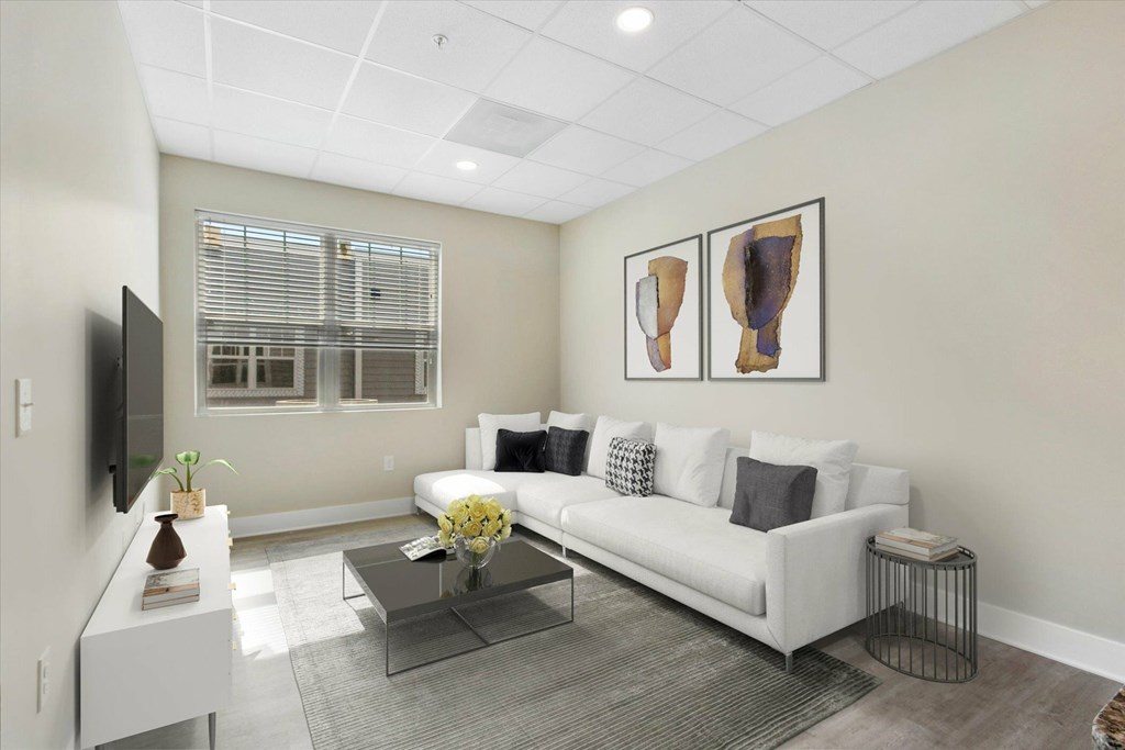 A living room with a white couch, a glass coffee table, and two framed artworks on the wall.