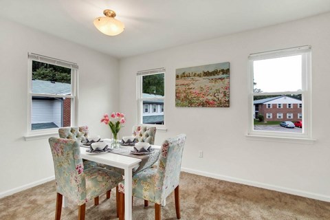 A dining room with a table set for four and a view of a house through the window.