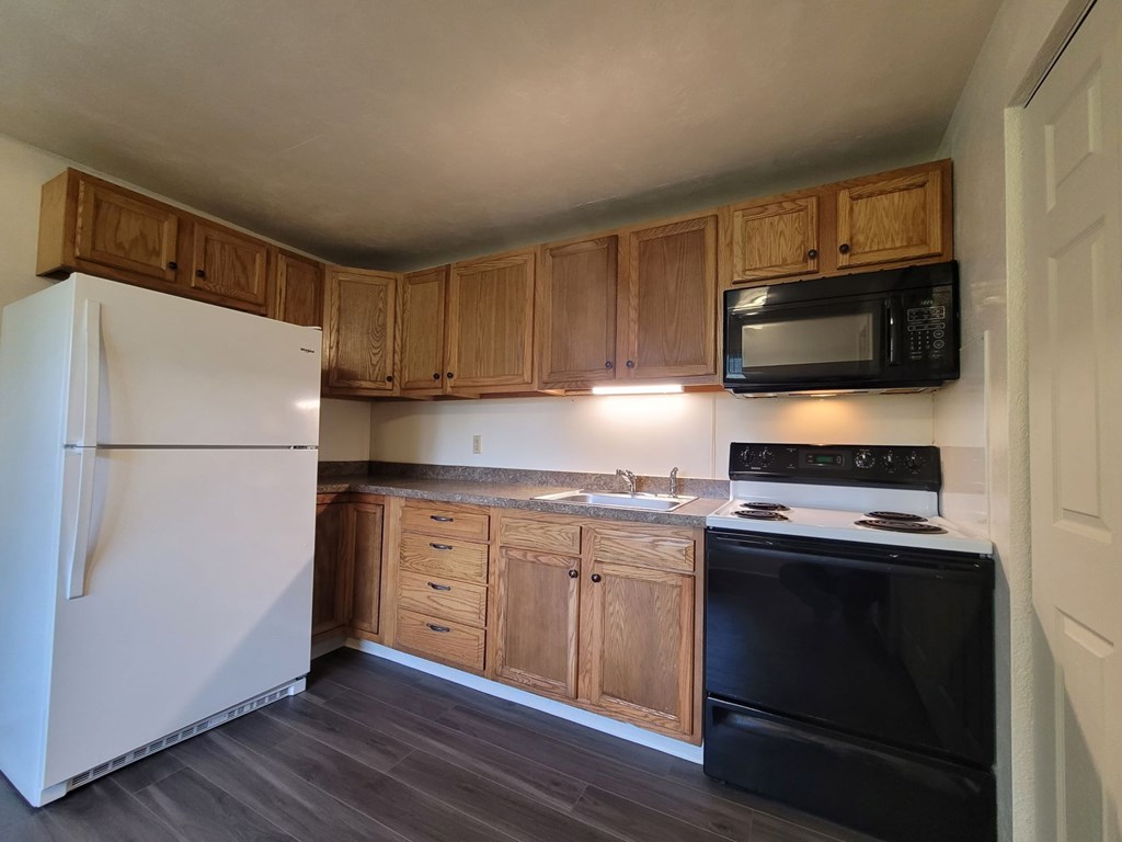 A kitchen with a white refrigerator, black oven, and wooden cabinets.