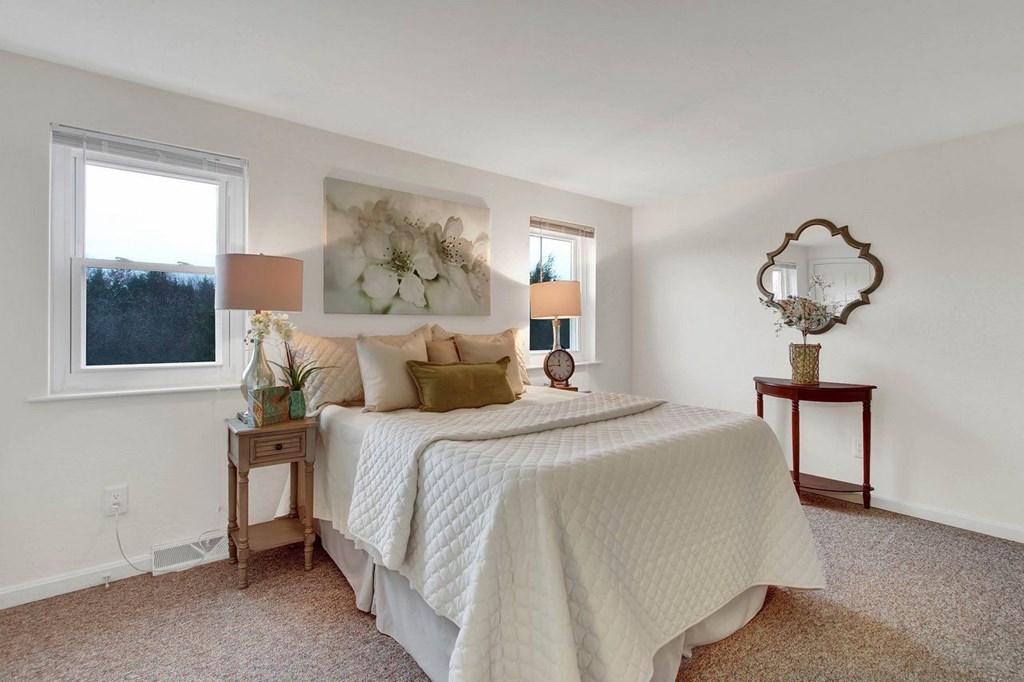 A bedroom with a bed, nightstand, and a table with a lamp.