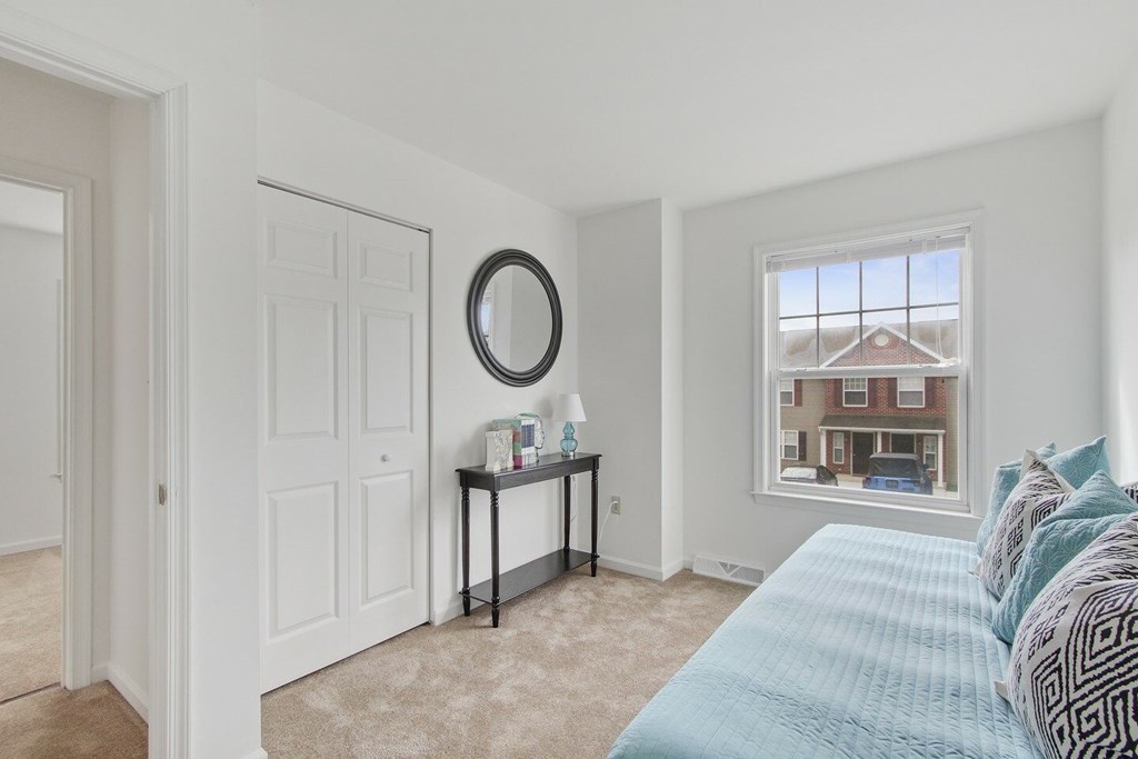A bedroom with a bed, a mirror, and a window overlooking a building.